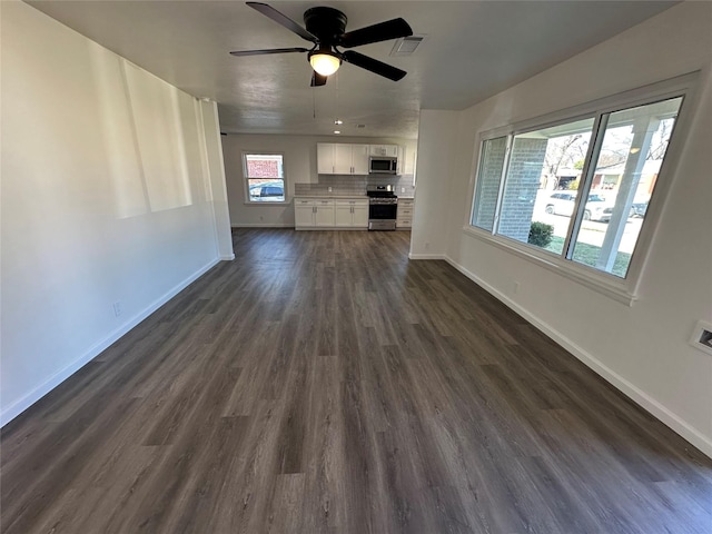 unfurnished living room with dark wood-type flooring, visible vents, ceiling fan, and baseboards