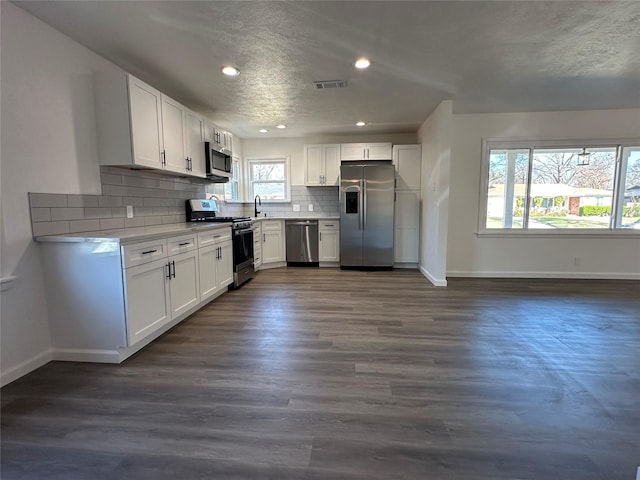 kitchen featuring appliances with stainless steel finishes, visible vents, white cabinetry, and tasteful backsplash