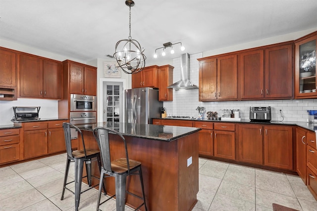 kitchen with a breakfast bar area, appliances with stainless steel finishes, glass insert cabinets, a kitchen island, and wall chimney range hood