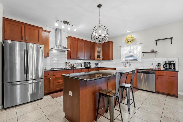 kitchen with light tile patterned flooring, a kitchen breakfast bar, appliances with stainless steel finishes, wall chimney range hood, and a center island