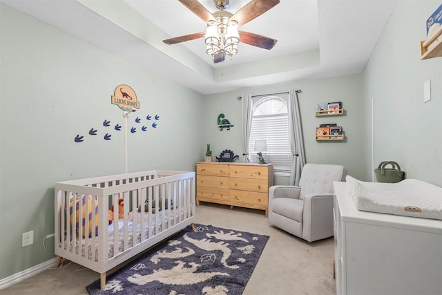 bedroom with light carpet, a crib, a raised ceiling, and a ceiling fan