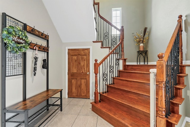 foyer featuring high vaulted ceiling, tile patterned flooring, and stairway