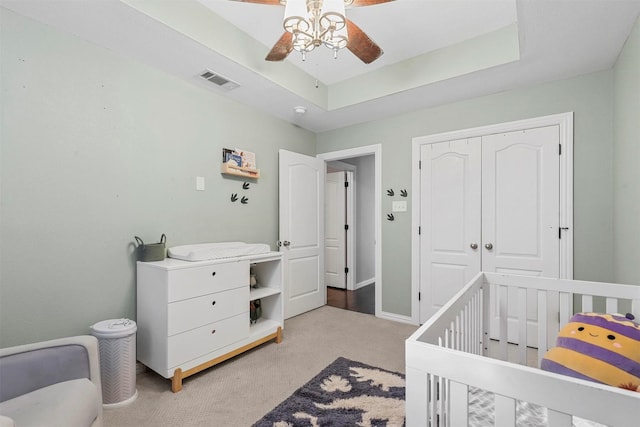 carpeted bedroom featuring a closet, a raised ceiling, visible vents, a ceiling fan, and baseboards