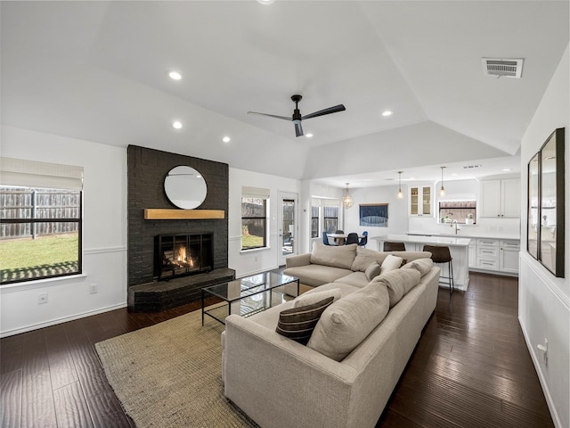 living area with vaulted ceiling, a fireplace, dark wood finished floors, and visible vents