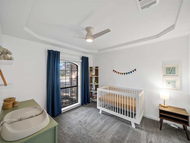 carpeted bedroom featuring a nursery area, ceiling fan, visible vents, and a raised ceiling