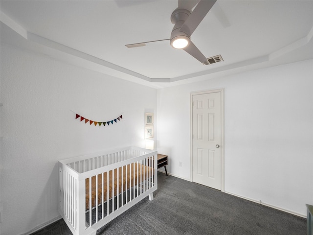 carpeted bedroom with a nursery area, ceiling fan, a tray ceiling, and visible vents