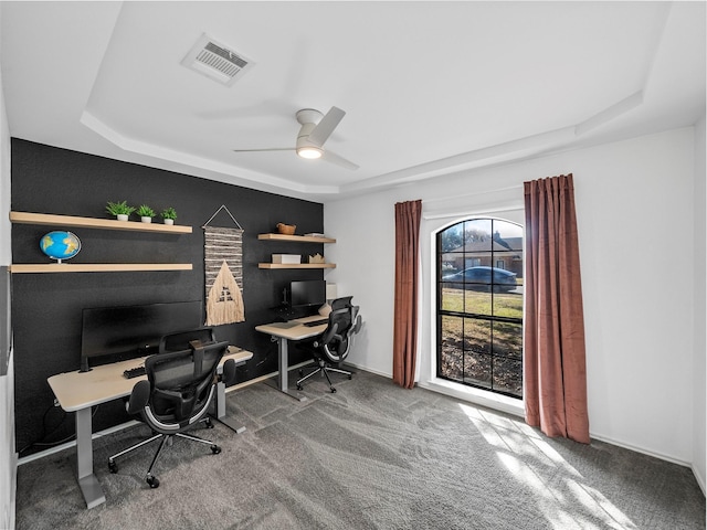 home office featuring carpet floors, visible vents, a raised ceiling, and a ceiling fan