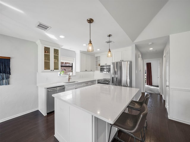 kitchen with visible vents, appliances with stainless steel finishes, white cabinets, a sink, and a kitchen island