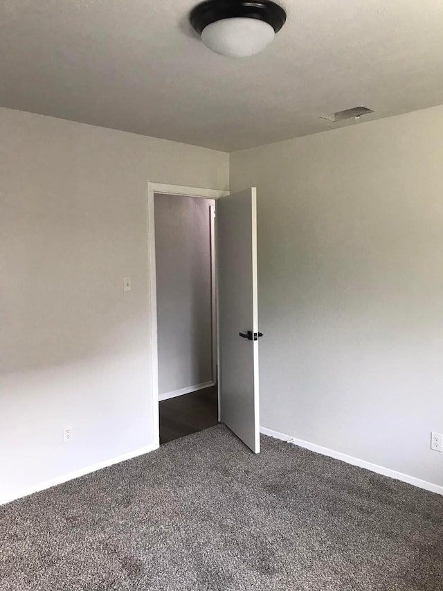 unfurnished room with baseboards, visible vents, and dark carpet