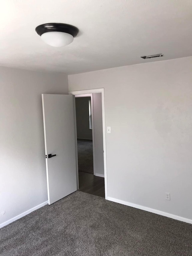 unfurnished room with visible vents, dark carpet, and baseboards