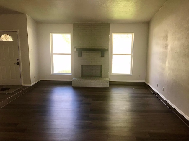 unfurnished living room featuring a brick fireplace, dark wood-style flooring, and baseboards