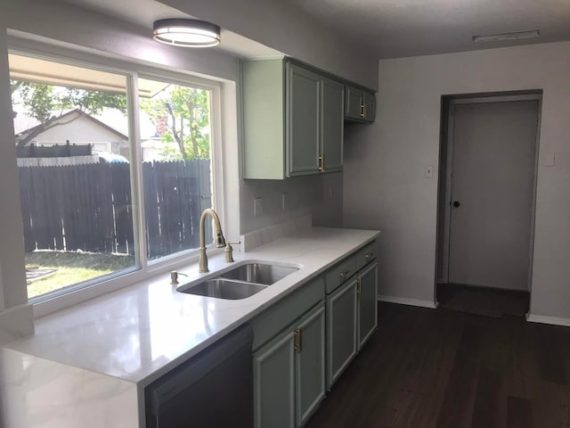 kitchen featuring a sink, baseboards, light countertops, dishwasher, and dark wood finished floors