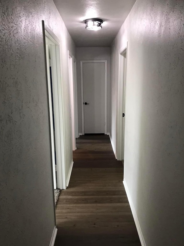 hallway with dark wood-style floors, baseboards, and a textured wall