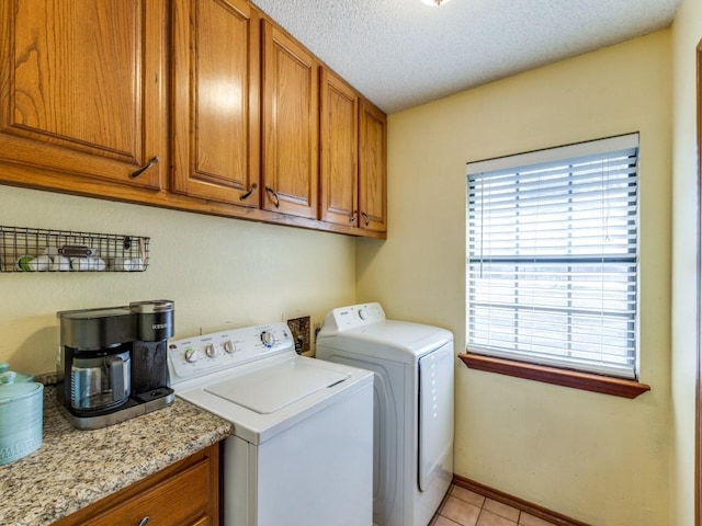 washroom with a textured ceiling, light tile patterned floors, baseboards, cabinet space, and washing machine and clothes dryer