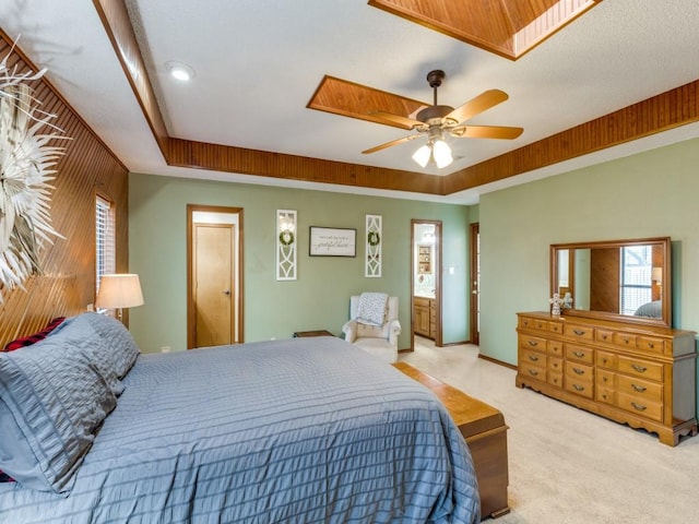 bedroom featuring light carpet, ceiling fan, a tray ceiling, and ensuite bathroom