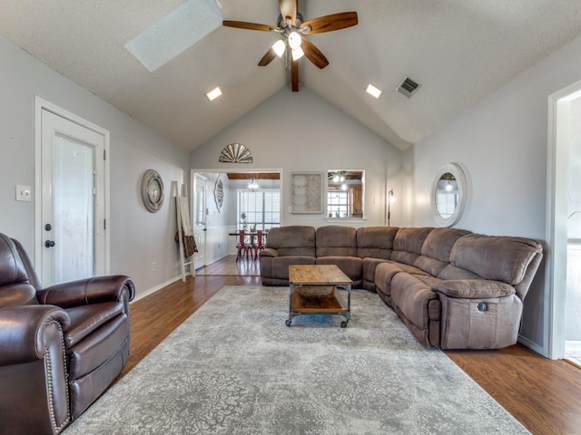 living area with visible vents, ceiling fan, wood finished floors, vaulted ceiling with skylight, and baseboards