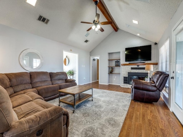 living area featuring a stone fireplace, wood finished floors, beam ceiling, and a healthy amount of sunlight