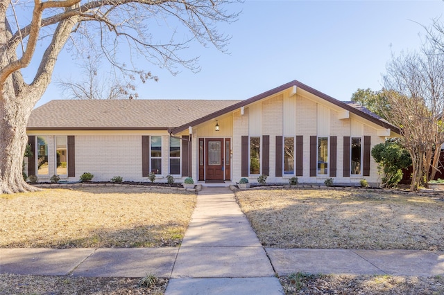 mid-century home featuring a shingled roof, a front lawn, and brick siding