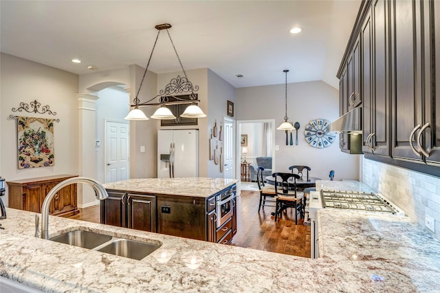 kitchen featuring light stone counters, dark wood-style flooring, a sink, refrigerator with ice dispenser, and decorative columns