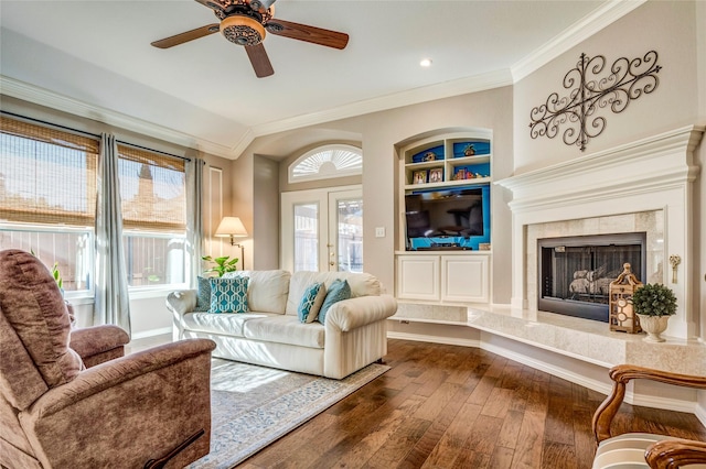 living room with built in shelves, a premium fireplace, baseboards, dark wood-style floors, and crown molding