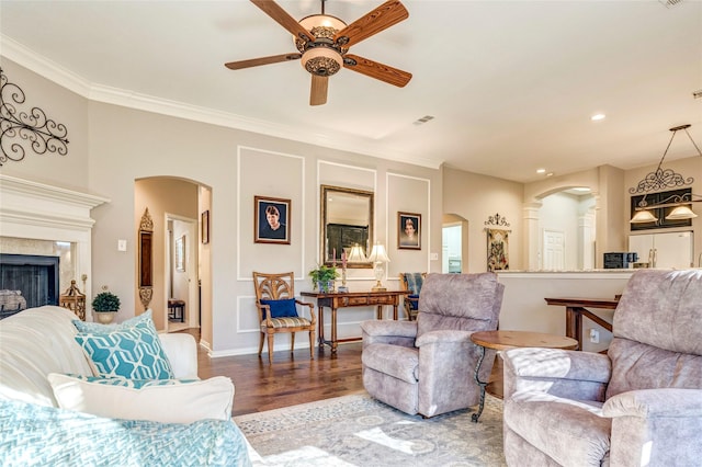 living area with arched walkways, wood finished floors, a ceiling fan, a high end fireplace, and crown molding