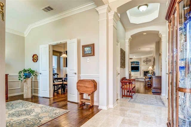 foyer featuring arched walkways, decorative columns, visible vents, ornamental molding, and hardwood / wood-style flooring