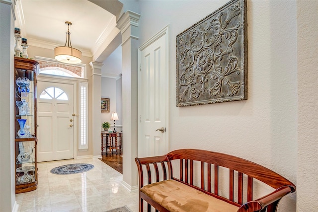 entryway featuring decorative columns, ornamental molding, baseboards, and a textured wall