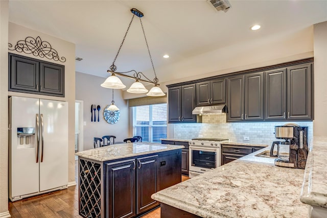 kitchen with under cabinet range hood, a kitchen island, visible vents, high end range, and white fridge with ice dispenser