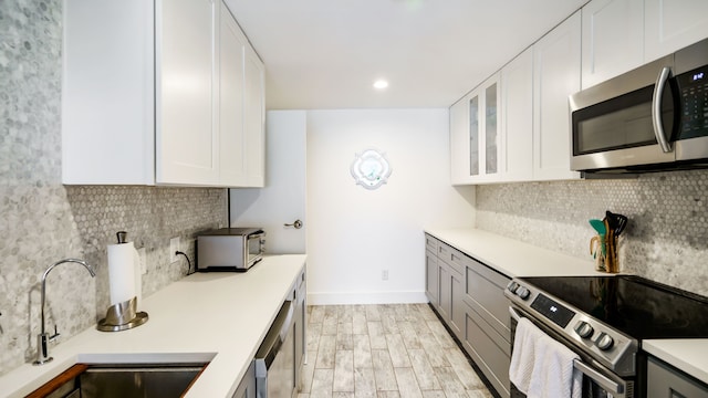 kitchen featuring decorative backsplash, appliances with stainless steel finishes, light countertops, white cabinetry, and a sink