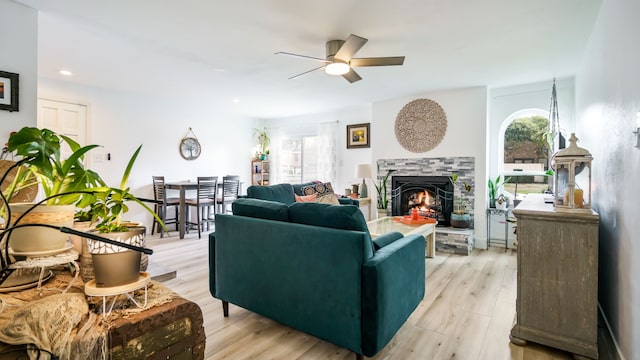 living area with light wood-type flooring, ceiling fan, a wealth of natural light, and a stone fireplace