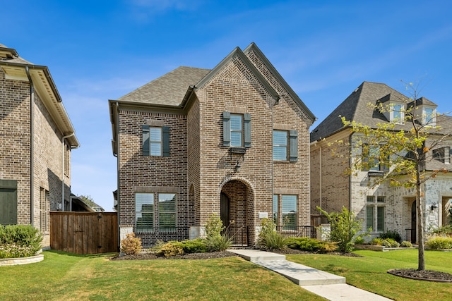 traditional-style home with a shingled roof, brick siding, and a front lawn