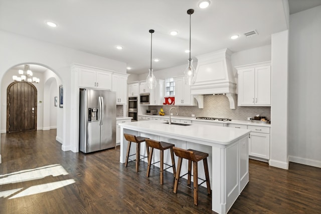 kitchen with arched walkways, stainless steel appliances, a sink, light countertops, and custom exhaust hood