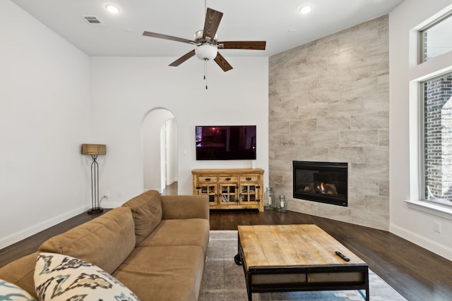 living room with baseboards, visible vents, arched walkways, a tile fireplace, and wood finished floors