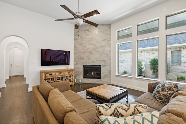 living area with baseboards, a tiled fireplace, arched walkways, and wood finished floors