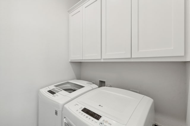 clothes washing area featuring separate washer and dryer and cabinet space