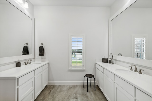 bathroom featuring baseboards, two vanities, a sink, and wood finished floors