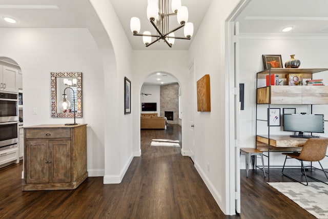 hallway featuring arched walkways, dark wood-style flooring, recessed lighting, an inviting chandelier, and baseboards