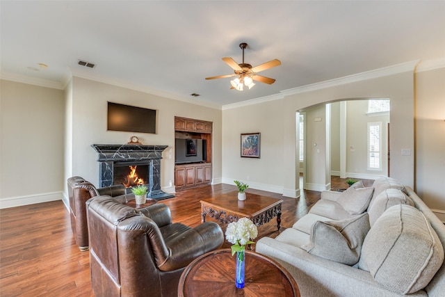 living room with a warm lit fireplace, visible vents, arched walkways, wood finished floors, and crown molding