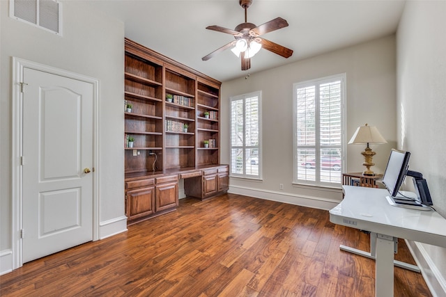 office featuring visible vents, baseboards, a ceiling fan, built in desk, and dark wood finished floors