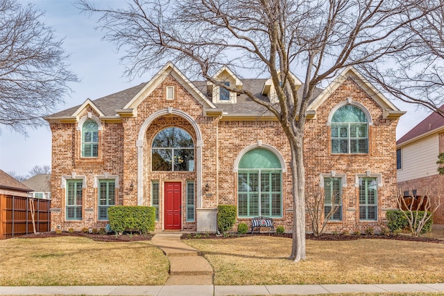 traditional-style house featuring roof with shingles, fence, a front lawn, and brick siding