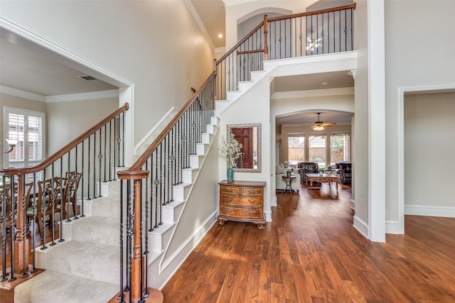 entrance foyer featuring arched walkways, visible vents, a towering ceiling, ornamental molding, and wood finished floors