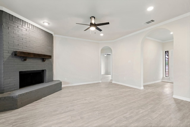 unfurnished living room featuring baseboards, visible vents, arched walkways, wood finished floors, and a brick fireplace