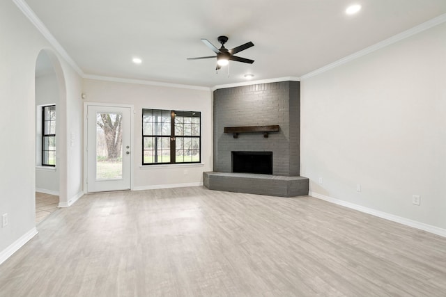 unfurnished living room featuring arched walkways, light wood-style flooring, ornamental molding, a brick fireplace, and baseboards