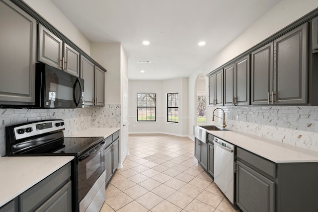 kitchen featuring light tile patterned floors, gray cabinetry, decorative backsplash, appliances with stainless steel finishes, and a sink