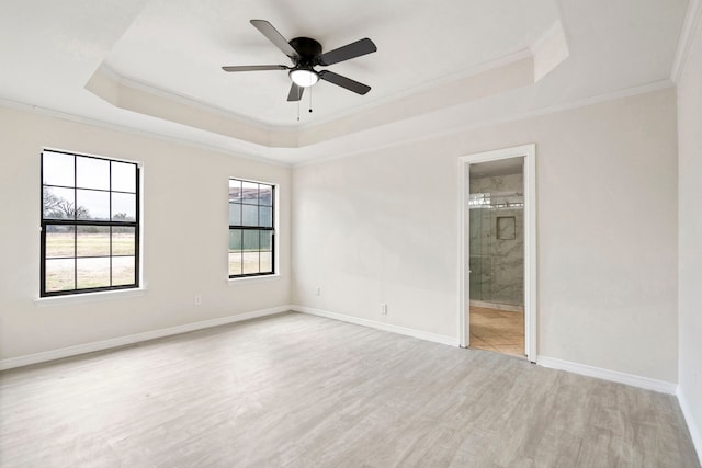 empty room featuring light wood-style flooring, a tray ceiling, and crown molding