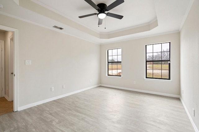 spare room with light wood finished floors, baseboards, a raised ceiling, a ceiling fan, and crown molding