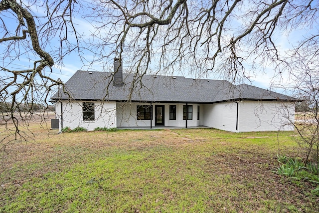 rear view of house with a shingled roof, a chimney, a lawn, and a patio