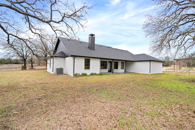 rear view of house with central AC, a yard, a chimney, and roof with shingles