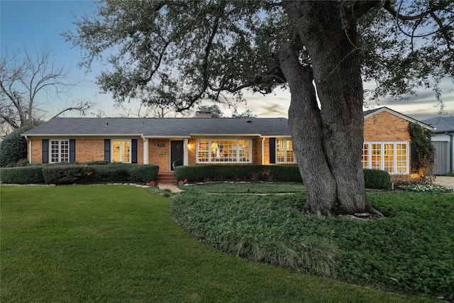 ranch-style house featuring brick siding, a chimney, and a front yard