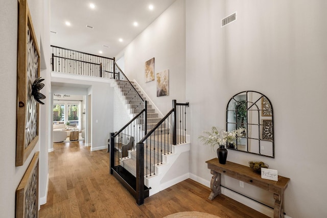 entrance foyer with baseboards, visible vents, wood finished floors, stairs, and a high ceiling